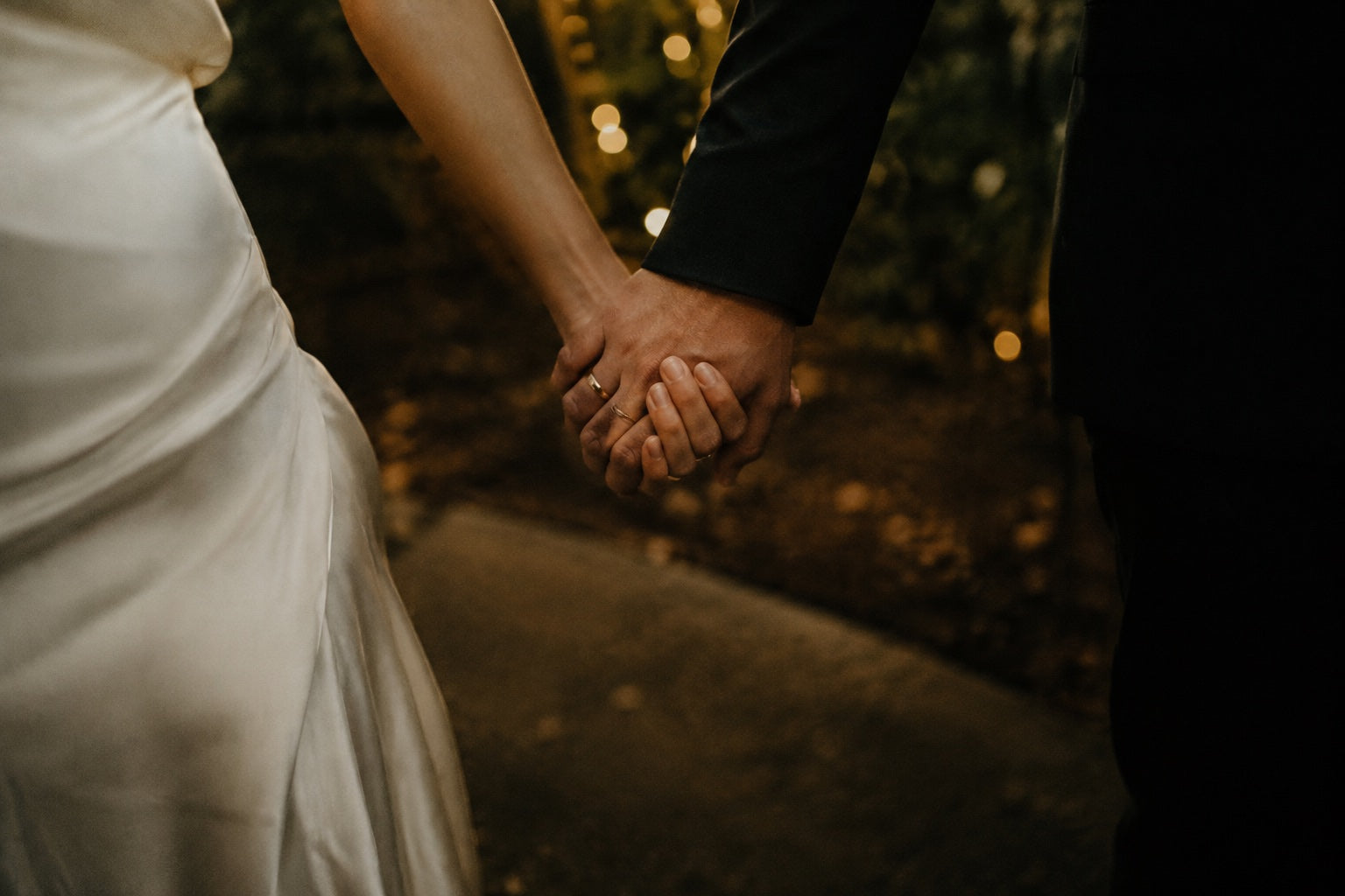 A wedding couple holding hands in the warm light of a garden.