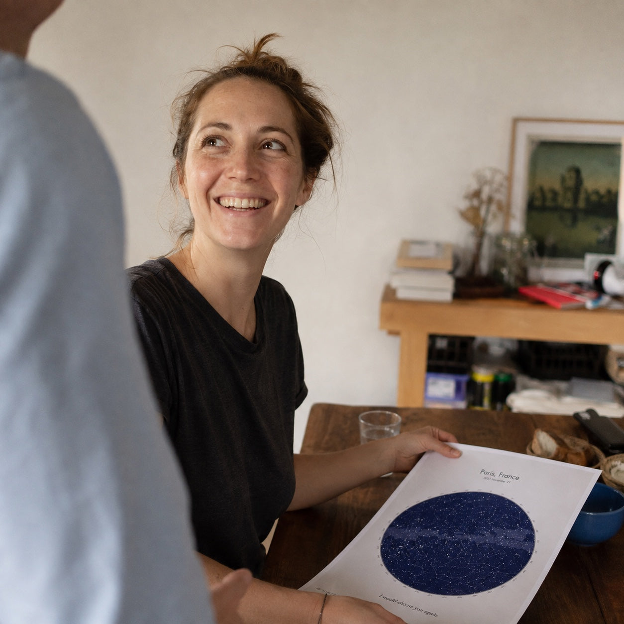 A woman smiling at her partner after receiving a personalized star map at their kitchen table.